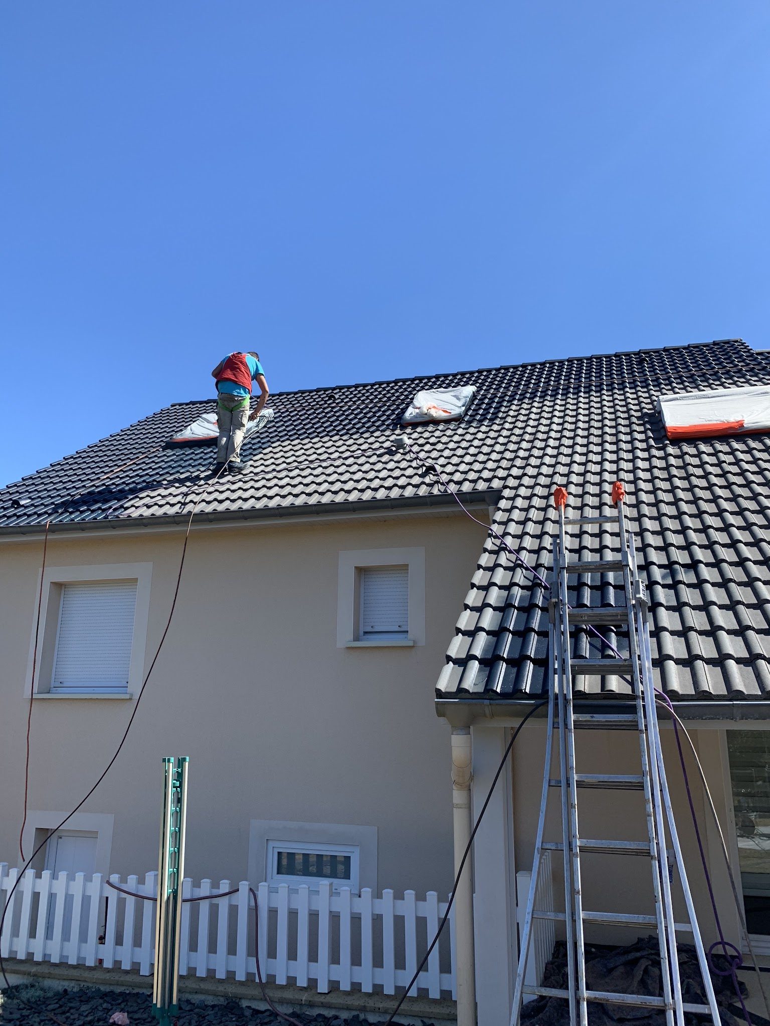 Un couvreur sur une toiture en tuiles noires, échelle posée